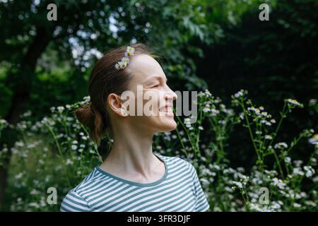 Donna sorridente con margherite tra i capelli che godersi la natura in un giardino Foto Stock