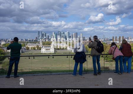 Visitatori sulla terrazza panoramica dell'Osservatorio Reale di Greenwich che ammirano e fotografano la Queen's House e lo skyline di Canary Wharf sotto le nuvole. Foto Stock