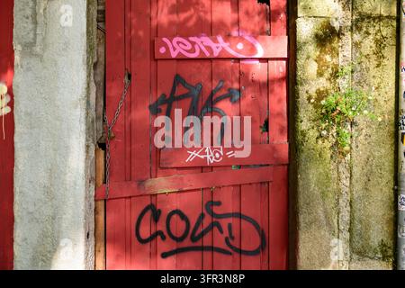 Oporto, Portogallo - 27 maggio 2019: Una porta di legno rossa coperta di graffiti e da un lucchetto è incorniciata da mura di pietra ricoperte di muschio a Oporto. Foto Stock