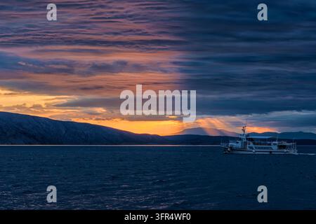 Una barca che naviga sul mare vicino a Senj con l'isola di Krk in lontananza sotto un cielo al tramonto. Foto Stock