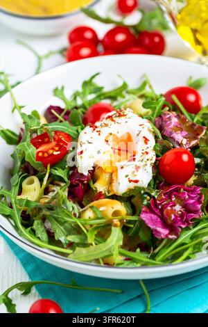 Insalata di rucola fresca, pomodorini, pasta e uovo benedict o poché primo piano Foto Stock