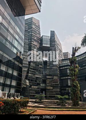 Torri d'ufficio moderne con facciate in vetro e cemento circondano un cortile paesaggistico con vegetazione tropicale. La scena trasmette un'atmosfera di business urbano contemporaneo Foto Stock