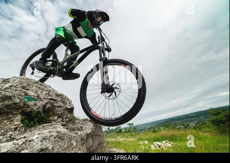 Un ciclista coraggioso scende le rocce. Sito di prova per mountain biker. Un ragazzo con protezioni guida fuoristrada, vista grandangolare dal basso Foto Stock