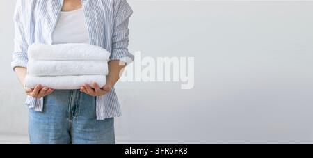 Una donna tiene tra le mani una pila di asciugamani bianchi puliti e ordinatamente piegati. Il concetto di lavaggio di pulizia e igiene. Tessuto di cotone organico senza Foto Stock