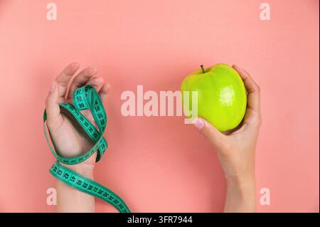 Una donna tiene in una mano una mela verde e nell'altra mano un metro a nastro, su uno sfondo rosa. Concetto di perdita di peso e dieta Foto Stock