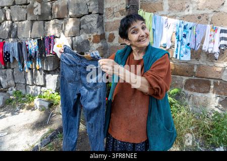Donna sorridente che tiene un paio di jeans davanti a biancheria stesa su una corda contro un muro di pietra, Yerevan, Yerevan, Armenia Foto Stock