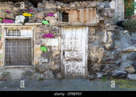 Facciata in pietra antica decorata con rocce dipinte a colori vivaci accanto a una porta di legno consumata e una finestra con inferriate, Yerevan, Yerevan, Armenia Foto Stock