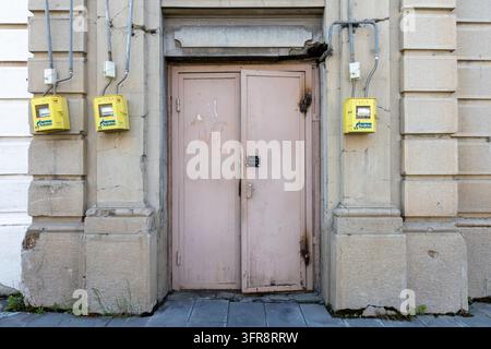 Antica porta in metallo affiancata da contatori del gas gialli su un muro di pietra crepato, provincia di Shirak, Gyumri, Armenia Foto Stock