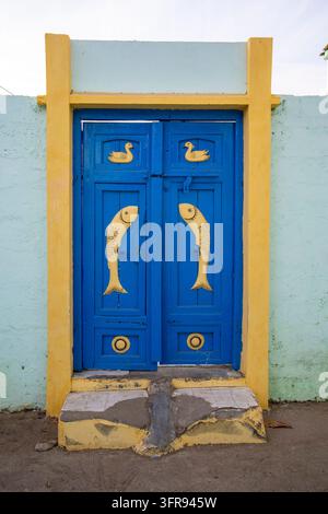 Doppia porta in legno blu decorata con motivi scolpiti di pesci e anatre gialli su un ingresso di casa, Gujarat, Mandvi, India Foto Stock