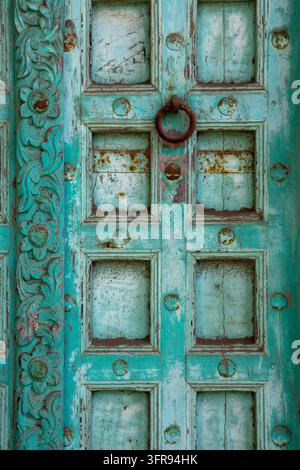 Una vista ravvicinata mostra una porta in legno intagliata turchese con un battente a forma di anello arrugginito, Gujarat, Mandvi, India Foto Stock