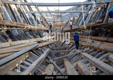 Operai della falegnameria si trovano su travi di legno all'interno della struttura complessa in legno dello scafo di una nave, Gujarat, Mandvi, India Foto Stock