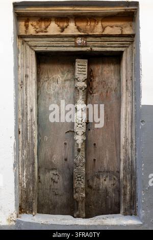 Porta in legno consumata con un montante centrale intagliato e una trabeazione in legno invecchiato, inserita in un muro imbiancato a calce e dipinto di grigio con una piccola targa numerata, Zanzibar Foto Stock