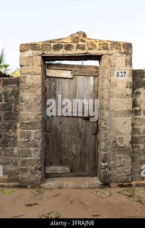 Antica porta di legno inserita in un muro di pietra consumato con un numero civico, Regione Marittima, Aneho, Togo Foto Stock