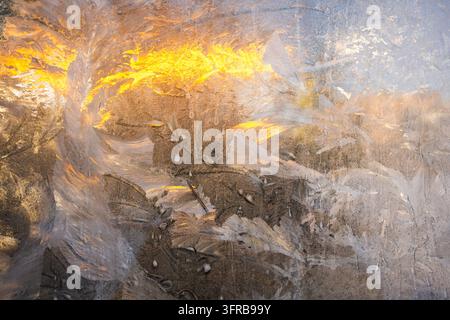 Disegni intricati di ghiaccio coprono il vetro della finestra congelato illuminato dalla calda luce del sole invernale all'aperto Foto Stock