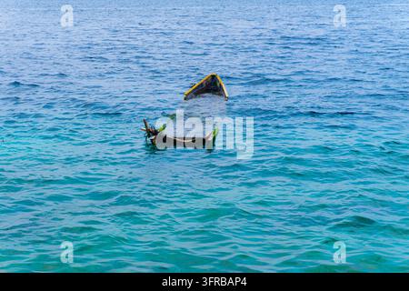 Barca di legno abbandonata semisommersa nel mare blu turchese con crescita verde sui bordi, la prua sopra l'acqua Foto Stock