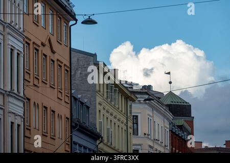 Edifici storici della città europea con facciate colorate, lampioni sospesi, tetti e drammatiche nuvole bianche su un cielo blu terso. Foto Stock