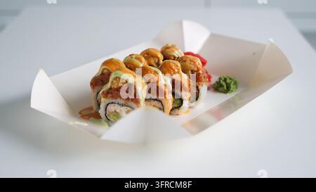 Rotoli di sushi con tonno, avocado e formaggio fresco, ricoperti di salse piccanti arancioni e verdi, serviti con zenzero sottaceto e wasabi Foto Stock