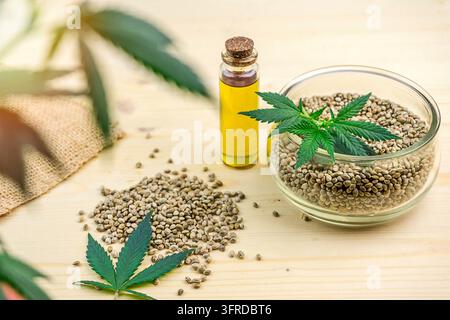 Semi di cannabis nella coppa olio di canapa CBD e sul tavolo E foglie di Cannabis Foto Stock