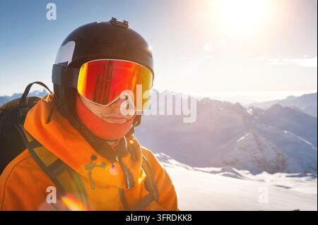 Un giovane uomo con occhiali da sci e casco su una pista da sci innevata e soleggiata. Ritratto di uno sportivo sicuro di sé Foto Stock