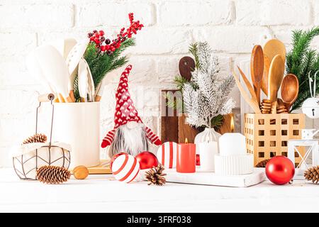 Un frammento di piano di lavoro in legno bianco con vari utensili da cucina e decorazioni natalizie. candele, palline, rami di abete Foto Stock