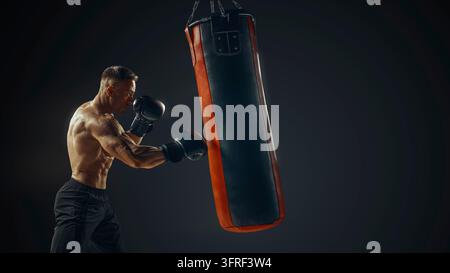 Boxer maschio che si allena con sacco da boxe isolato. Giovane boxer attraente che si allena sul sacco da boxe. Boxer maschio che si allena prima del combattimento. Boxer colpisce il sacco Foto Stock