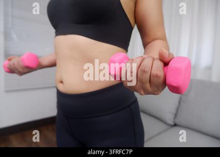 Giovane donna asiatica che fa esercizio a casa con un manubrio per allenare braccia e parte superiore del corpo Foto Stock