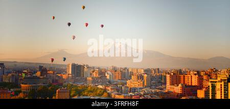 Paesaggio urbano all'alba con mongolfiere che fluttuano sopra. La montagna innevata Nemrut si erge dietro lo skyline urbano. La luce calda proietta un bagliore dorato su b Foto Stock