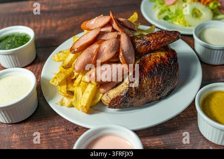 Pollo a la brasa tradizionale peruviana con patatine fritte e salsicce, servito con salse e insalata fresca. Foto Stock