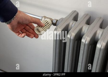Primo piano di una mano che tiene una manopola di controllo a costolature bianche su un radiatore in ghisa Foto Stock