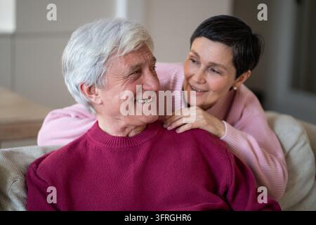 Coppia di anziani amorevoli e felici, uomo e donna, che si abbracciano e sorridono mentre si rilassano insieme a casa. Foto Stock