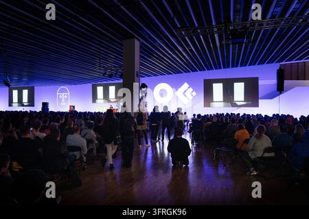 PUBBLICO CHE GUARDA UNA PRESENTAZIONE A UN FESTIVAL DI DESIGN, BARCELONA OFFF FESTIVAL 2019 REPORTAGE, BARCELONA, SPAGNA: Un vasto pubblico è seduto in una sala buia, guardando una presentazione su uno schermo largo illuminato da luci blu e viola e loghi grafici durante un festival. INFO: La conferenza OFFF è stata lanciata nel 2001 ed è la più grande vetrina mondiale della creatività visiva contemporanea e del design. Attira i migliori designer, artisti, registi e fotografi del mondo. Serve come piattaforma globale per lo scambio e la collaborazione creativa. Foto Stock