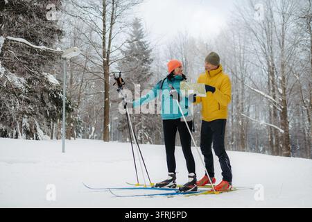 Coppia di anziani su sci di fondo in piedi in una foresta innevata e leggono una mappa insieme. Foto Stock