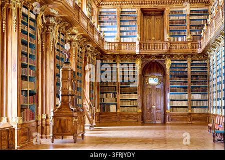 Scaffali in noce barocchi con intarsi dorati e una linea di galleria superiore rivestono la sala storica della biblioteca monastica a Hradčany, Repubblica Ceca. Foto Stock