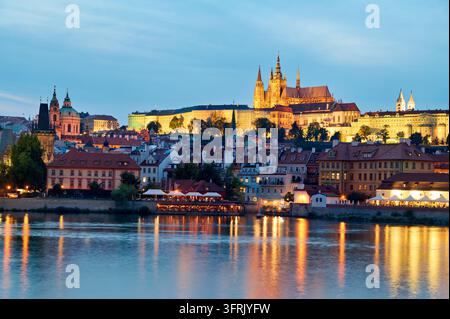 Cattedrale di San Vito e il quartiere di Mala Strana illuminati al crepuscolo estivo, con i ristoranti sul lungofiume riflessi nell'acqua, Praga. Foto Stock