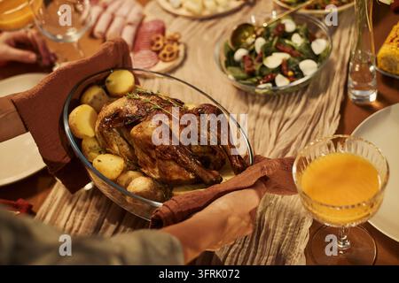 Donna che porta un pollo intero al forno al tavolo festivo a casa Foto Stock
