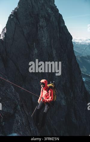 Arrampicatore in giacca rossa che si cala lungo una parete rocciosa Foto Stock