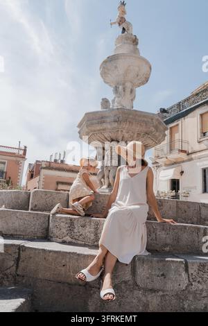 Madre e figlia sedute sui gradini di un'antica fontana europea Foto Stock