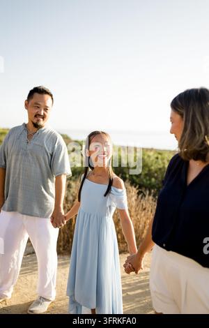 Famiglia asiatica sorridente che si tiene per mano durante una passeggiata all'aperto Foto Stock