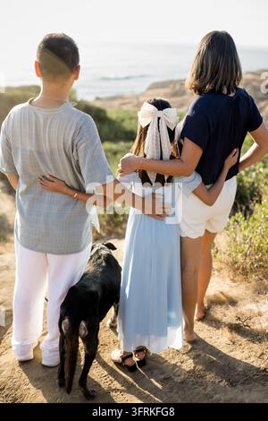 Famiglia con cane che si abbraccia e guarda il panorama dell'oceano Foto Stock