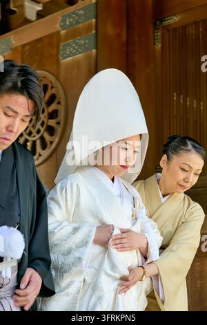 Una sposa con un cappuccio wataboshi è assistita da un'assistente accanto allo sposo durante una cerimonia nuziale tradizionale in un santuario di legno a Tokyo, Giappone Foto Stock