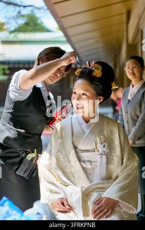 Un parrucchiere aggiusta l'acconciatura tradizionale kanzashi di una sposa giapponese prima di una cerimonia nuziale shintoista, mentre un'assistente osserva. Foto Stock