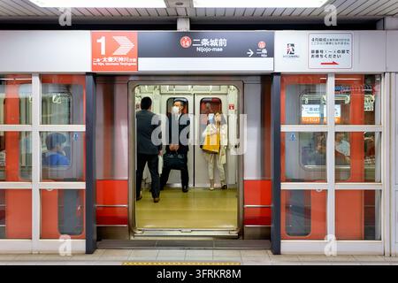 I pendolari si trovano in un vagone dietro le porte aperte dei parabordi della metropolitana comunale di Kyoto in Giappone, un uomo indossa una mascherina. Foto Stock