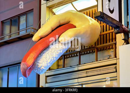 Un pugno scolpito sovradimensionato che stringe una fetta di tonno sul riso pende sopra una facciata di ristorante in Giappone al crepuscolo. Foto Stock