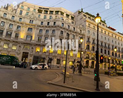 MADRID, SPAGNA - 09 OTTOBRE 2026 Gli edifici ornati di Madrid brillano al crepuscolo, con negozi illuminati e lampioni sotto i fili del tram. Furgone di consegna CORLINA Foto Stock