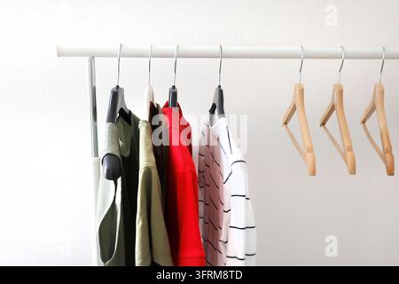 Magliette casual basic appese su una mensola di casa con grucce di legno vuote nella stanza. Organizzazione consapevole dello stile di vita sostenibile, vita semplice. Guardaroba capsule Foto Stock