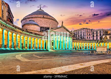 Le luci illuminano la cupola della basilica e la colonnata curva accanto a una statua equestre in una serata invernale al crepuscolo a Napoli, Campania, Italia. Foto Stock