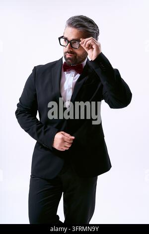 Un uomo vestito con un elegante completo nero e un farfallino sistema gli occhiali con uno sguardo sicuro. Foto Stock
