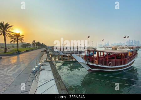 Paesaggio urbano e skyscapers del centro città visto attraverso tradizionali dhow barche a Corniche a Doha, Qatar al tramonto Foto Stock