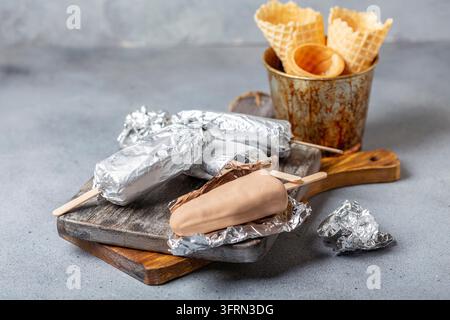 Gelato artigianale su un bastoncino avvolto in carta stagnola su un vassoio di servizio in legno, messa a fuoco selettiva Foto Stock