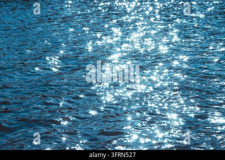 Foto ravvicinata di una superficie d'acqua blu scintillante con riflessi solari brillanti, riflessi di luce e leggere increspature. Perfetto per uno sfondo astratto Foto Stock